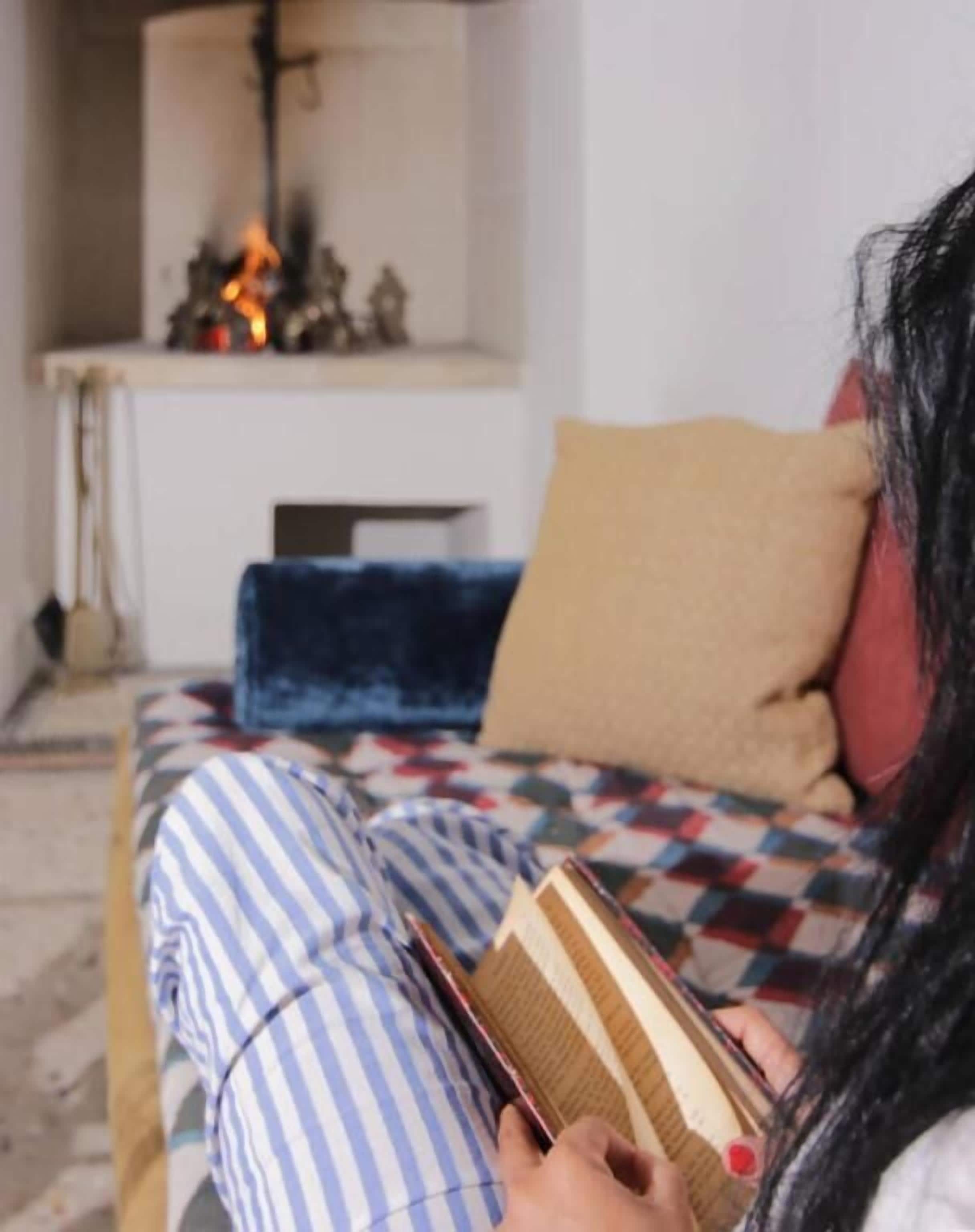 Eine Person sitzt auf einem Bett mit gestreifter Bettwäsche und liest ein Buch.
