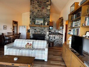 A cozy living room with a stone fireplace, a plaid sofa, a wooden coffee table, and a bookshelf filled with books.