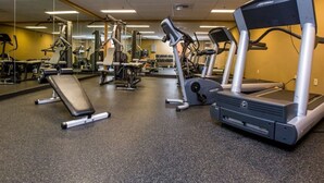 Een fitnessruimte met loopbanden, krachtapparaten en een bank.