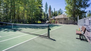An outdoor tennis court with a net, surrounded by trees and a fence. - Mountain Harbor #114 3 Bedroom Condo (Whitefish)