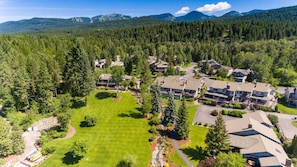 A residential area with multiple houses, a large lawn, and a forested backdrop. - Mountain Harbor #114 3 Bedroom Condo (Whitefish)