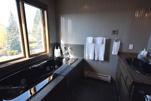 A modern bathroom with a large window, a black bathtub, and a tiled shower area. - Mountain Harbor #114 3 Bedroom Condo (Whitefish)