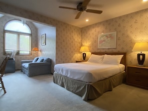 A bedroom with a bed, two bedside lamps, a ceiling fan, a chair, a desk, and a window with blinds. - Mountain Harbor #114 3 Bedroom Condo (Whitefish)