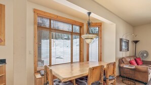 A dining area with a wooden table and chairs, a ceiling fan, and a window with blinds. - Black Diamond 3 Bedroom Condo (Whitefish)