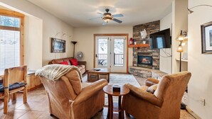 A cozy living room with a fireplace, leather chairs, a wooden coffee table, and a ceiling fan. - Black Diamond 3 Bedroom Condo (Whitefish)