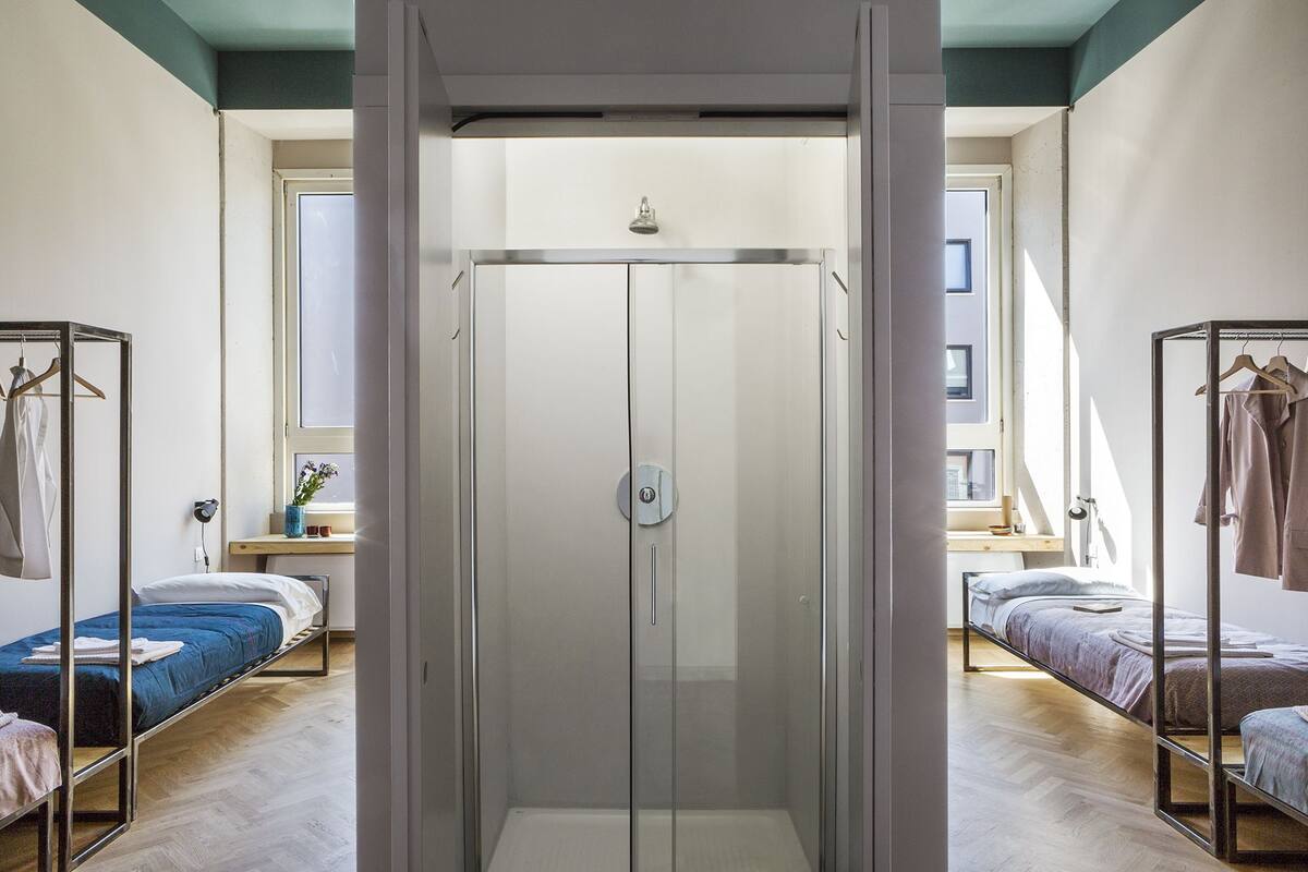 A modern bedroom with a glass shower enclosure, two beds, and a wardrobe.