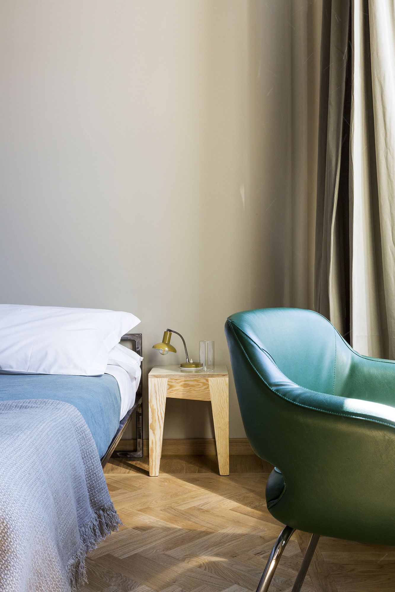 Un dormitorio con cama, una mesita de noche con lámpara, una silla y suelo de madera.