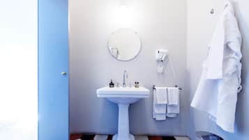 Un baño con lavamanos pedestal blanco, un espejo redondo y un perchero con varias toallas.