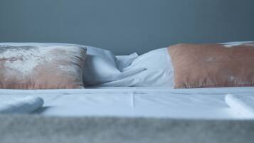 Ein Bett mit weißer Bettwäsche und zwei Kissen, eines mit braun-weißer Musterung.