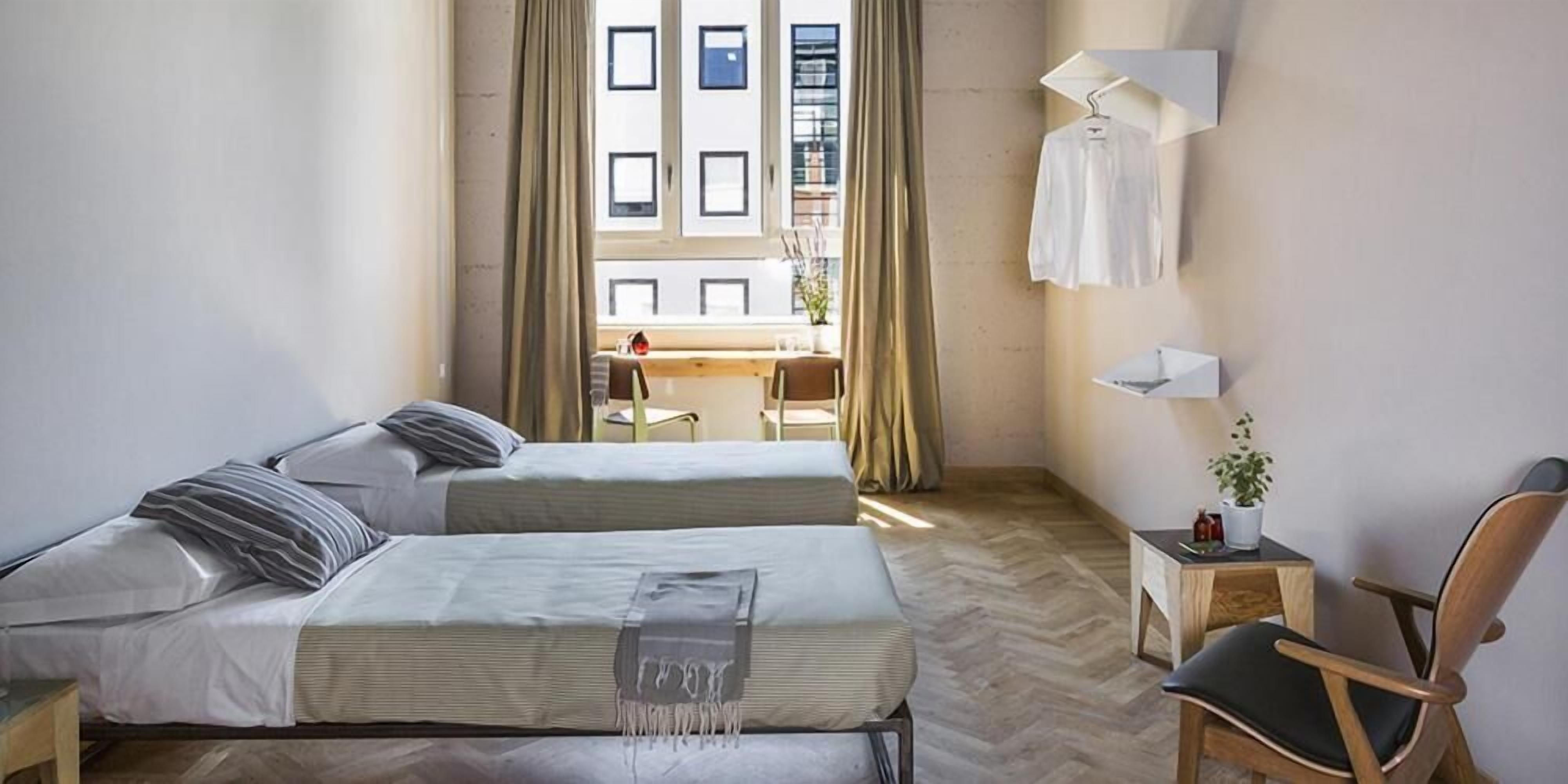 Una habitación de hotel moderna con dos camas, un escritorio, una silla y una planta en maceta.