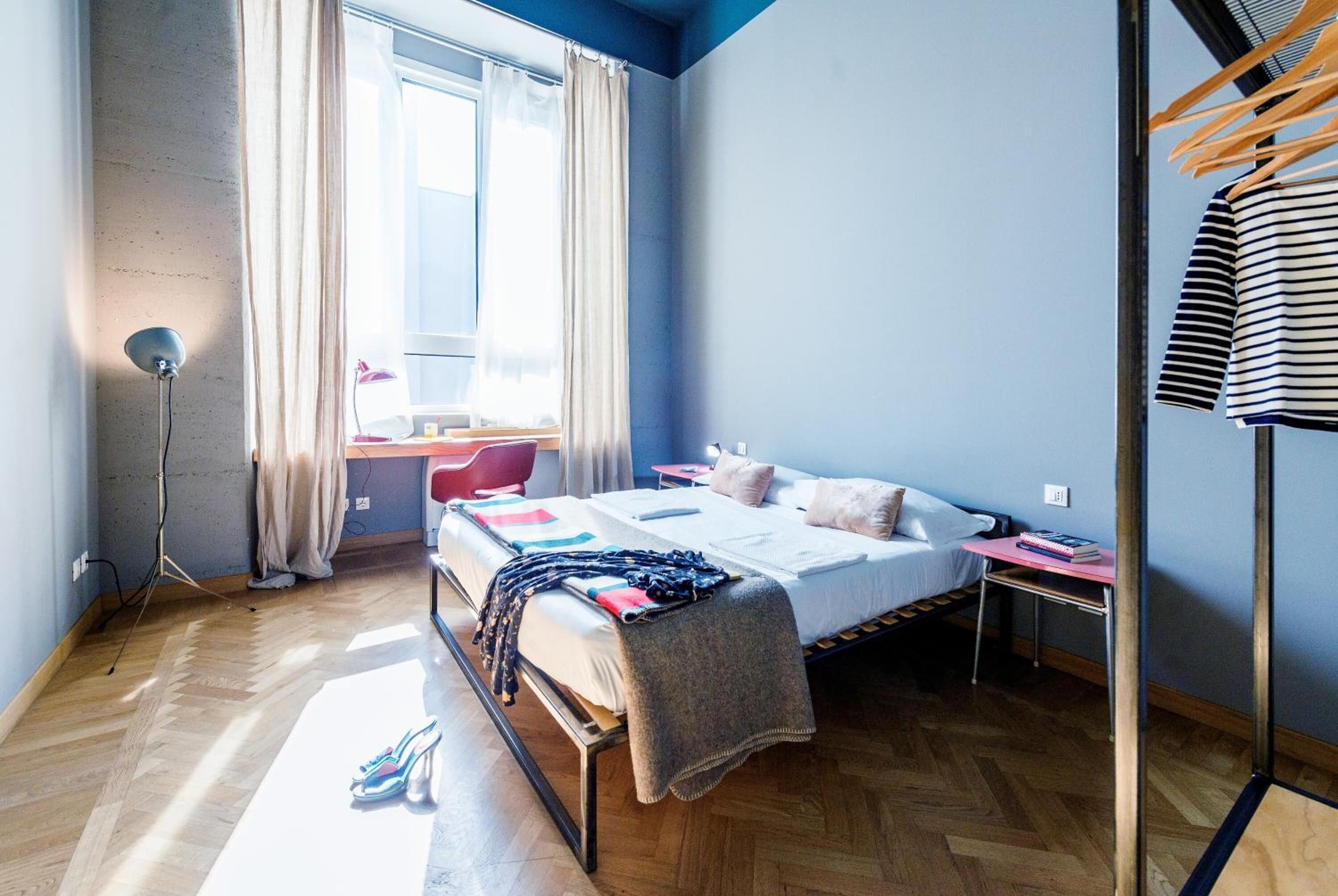 Un dormitorio con cama, mesita de noche y ventana con cortinas.