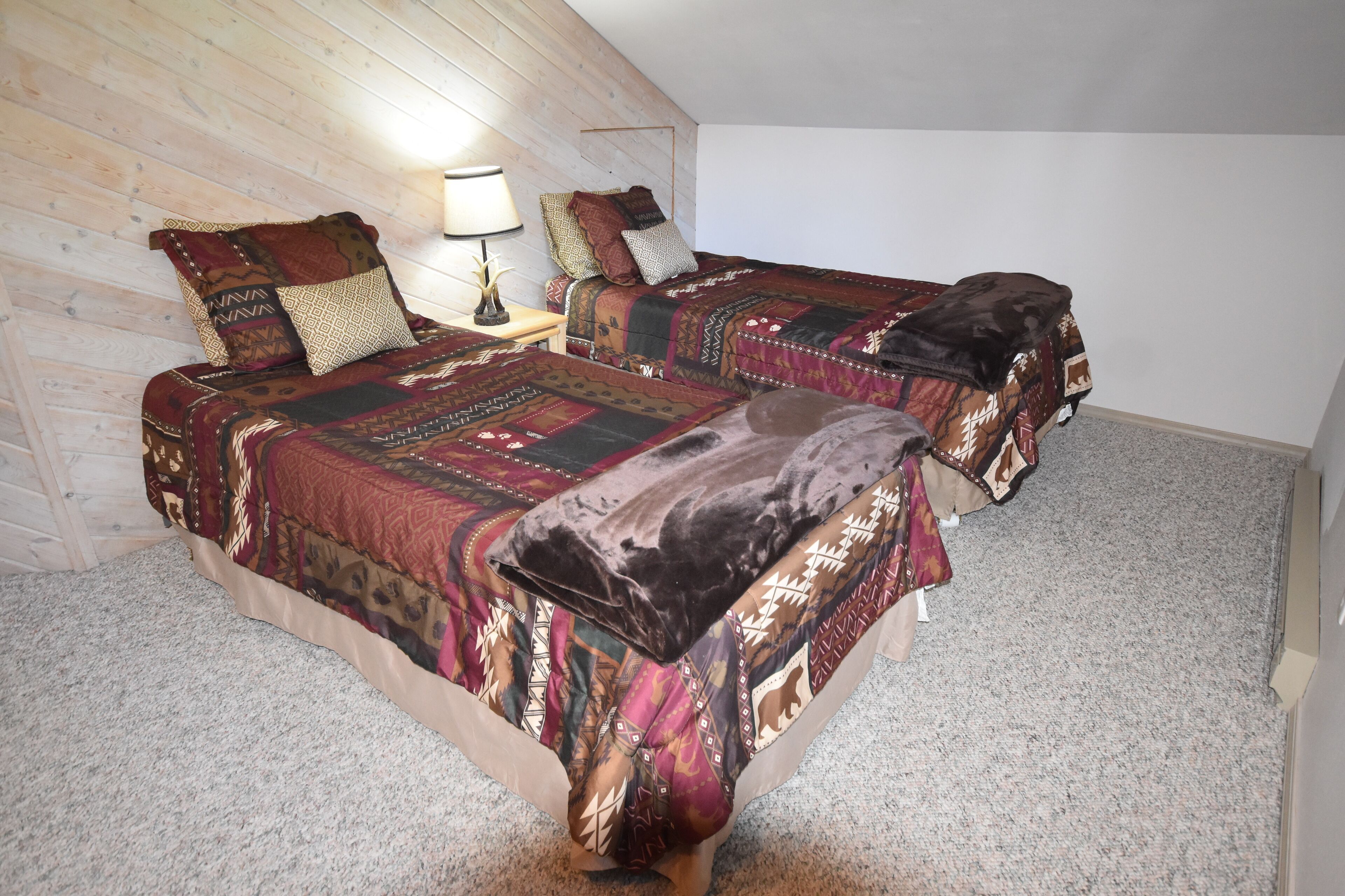 A bedroom with two beds, each with patterned bedding and a nightstand with a lamp.