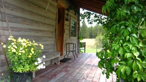 A wooden porch with a bench, a potted plant with yellow flowers, and a view of a grassy field.