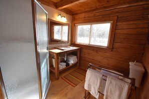 Une salle de bain rustique, avec des murs en bois, un meuble-lavabo en bois, un évier, un miroir, une fenêtre et un porte-serviettes.