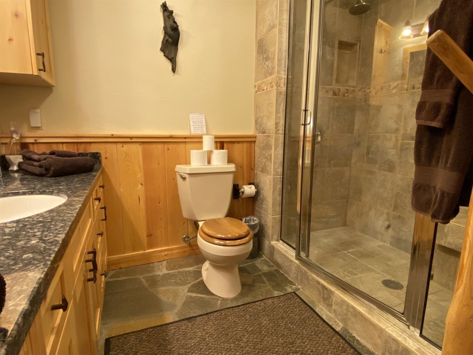 Een badkamer met een houten wastafelmeubel, een toilet, een douche met glazen deuren en een handdoekrek.