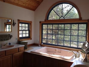 A bathroom with a large window, wooden cabinets, a sink, and a bathtub.
