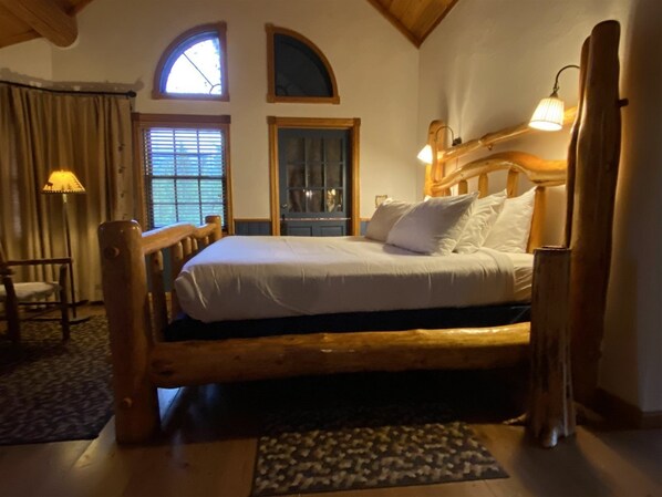 A wooden bed with white linens in a room with a sloped ceiling and a window with blinds.