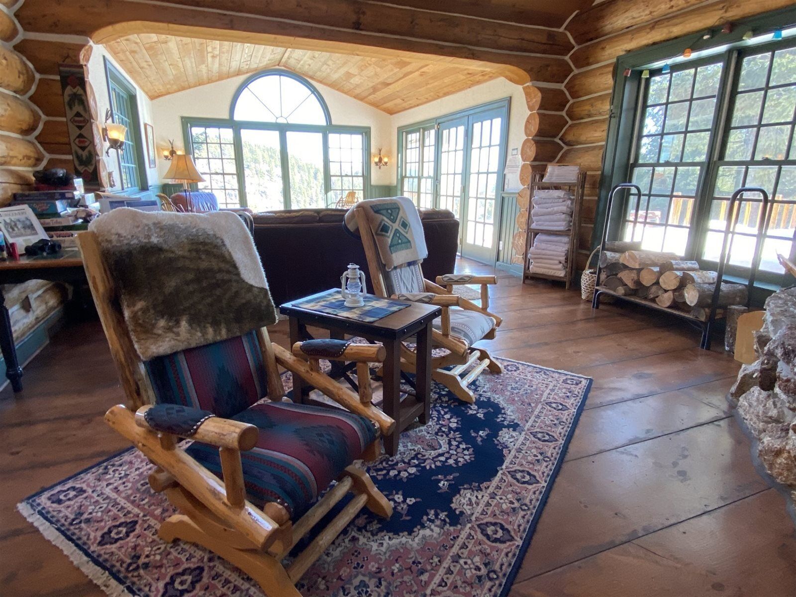 A cozy log cabin interior with wooden furniture, a large window, and a fireplace.