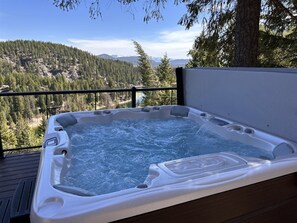 A hot tub on a wooden deck with a view of a forested mountain range.