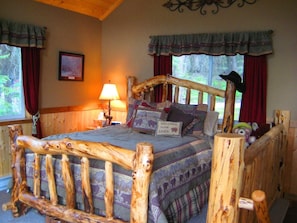 A rustic cabin-style bedroom with a wooden bed frame, a lamp, and a 'Welcome to our cabin' pillow. - Ashley Lake 1 Bedroom Cabin (Kalispell)