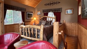 A cozy cabin room with a wooden bed, red leather chairs, and a ceiling fan.