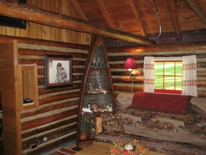 A cozy log cabin interior with a wooden ceiling, a framed photograph, a lamp, and a window with curtains. - Ashley Lake 1 Bedroom Cabin (Kalispell)