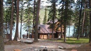 A cabin with a stone fireplace, surrounded by a forest and a lake.