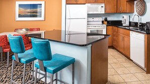 A modern kitchen with a central island, bar stools, wooden cabinets, and a microwave.