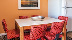 A dining area with a white table, red patterned chairs, a silver bowl, and a framed picture on the wall.