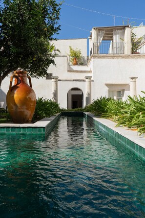 A pool with a large vase, a white building with columns, and a clear sky. - Palazzo Muci (Nardò)