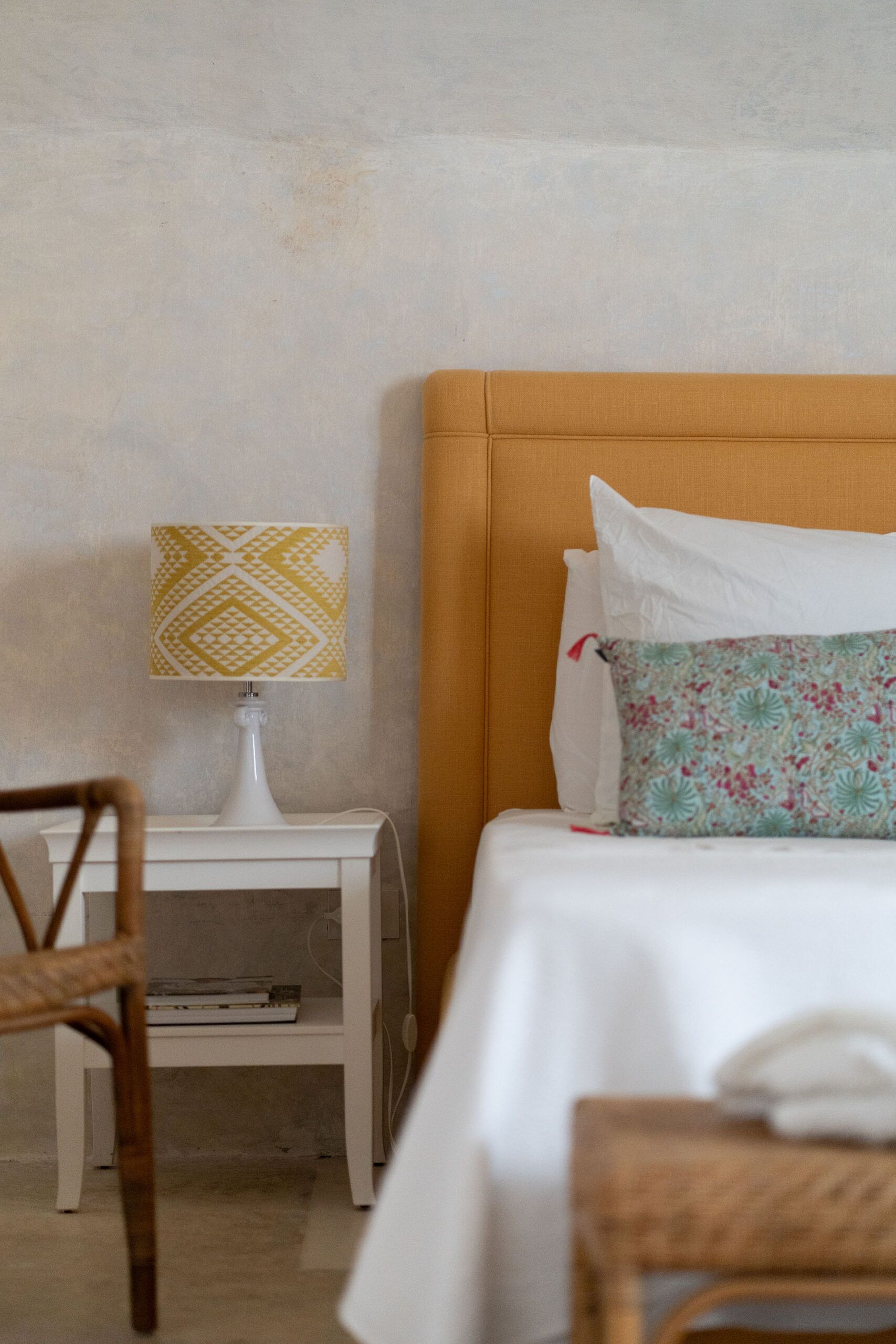 A bedroom with a bed, a nightstand, a lamp, and a chair.