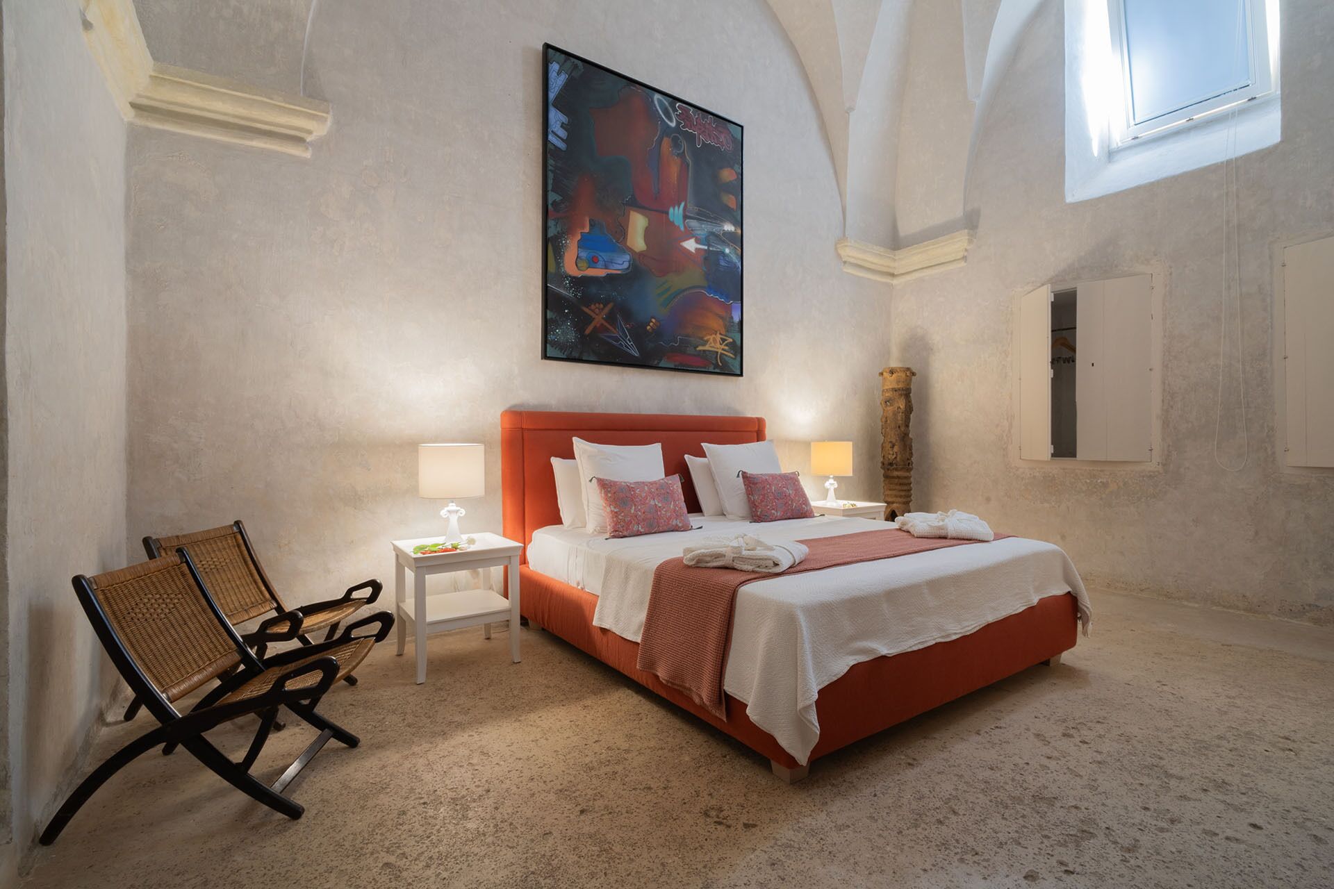 Un dormitorio con una cama grande, dos mesitas de noche, una silla y un cuadro en la pared.