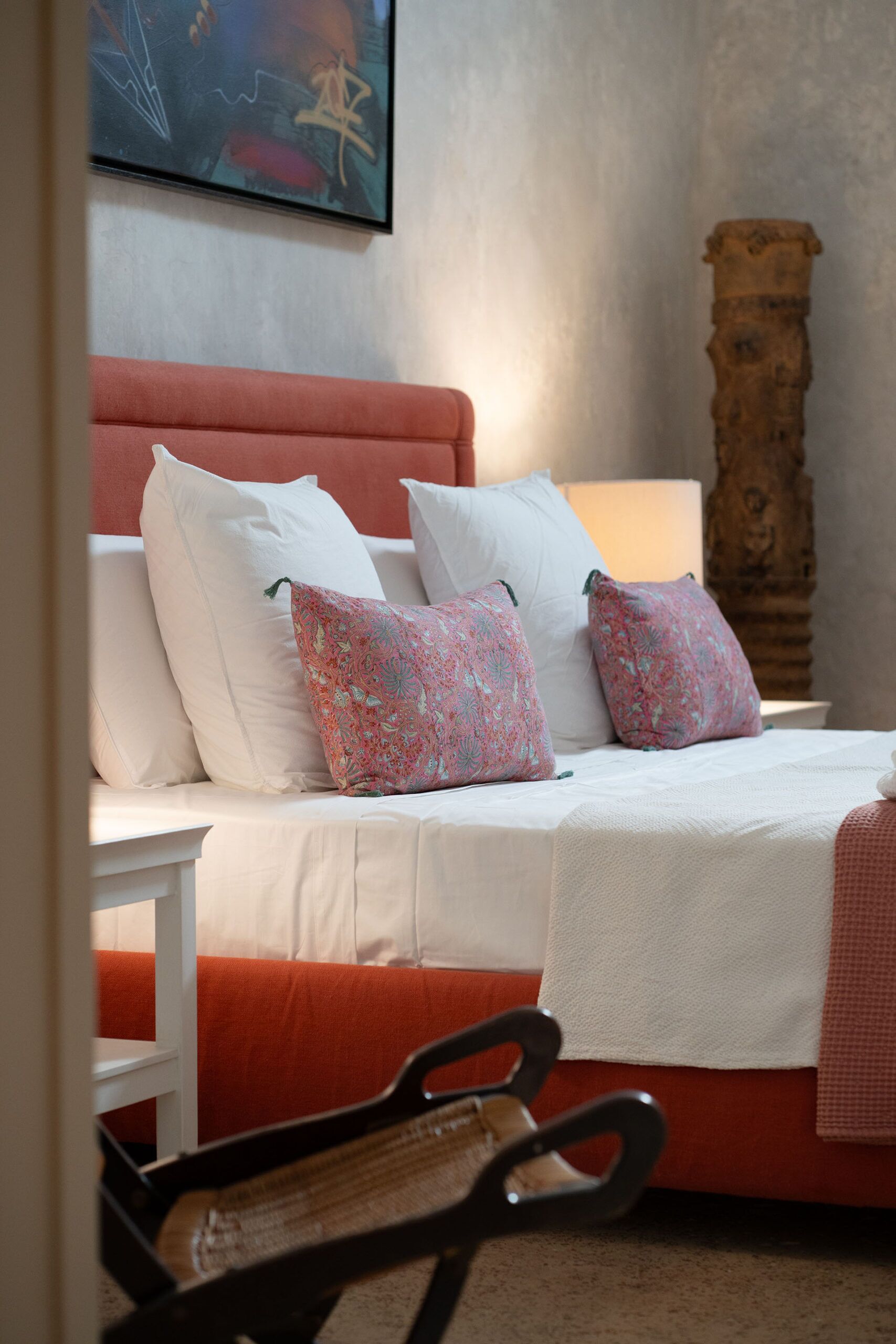 A bed with white and pink floral pillows, a wooden headboard, and a white bedside table.