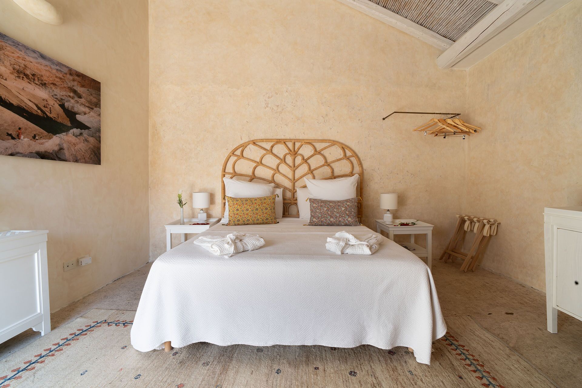 Une chambre à coucher avec un grand lit, deux tables de chevet, une lampe fixée au mur et un tableau.