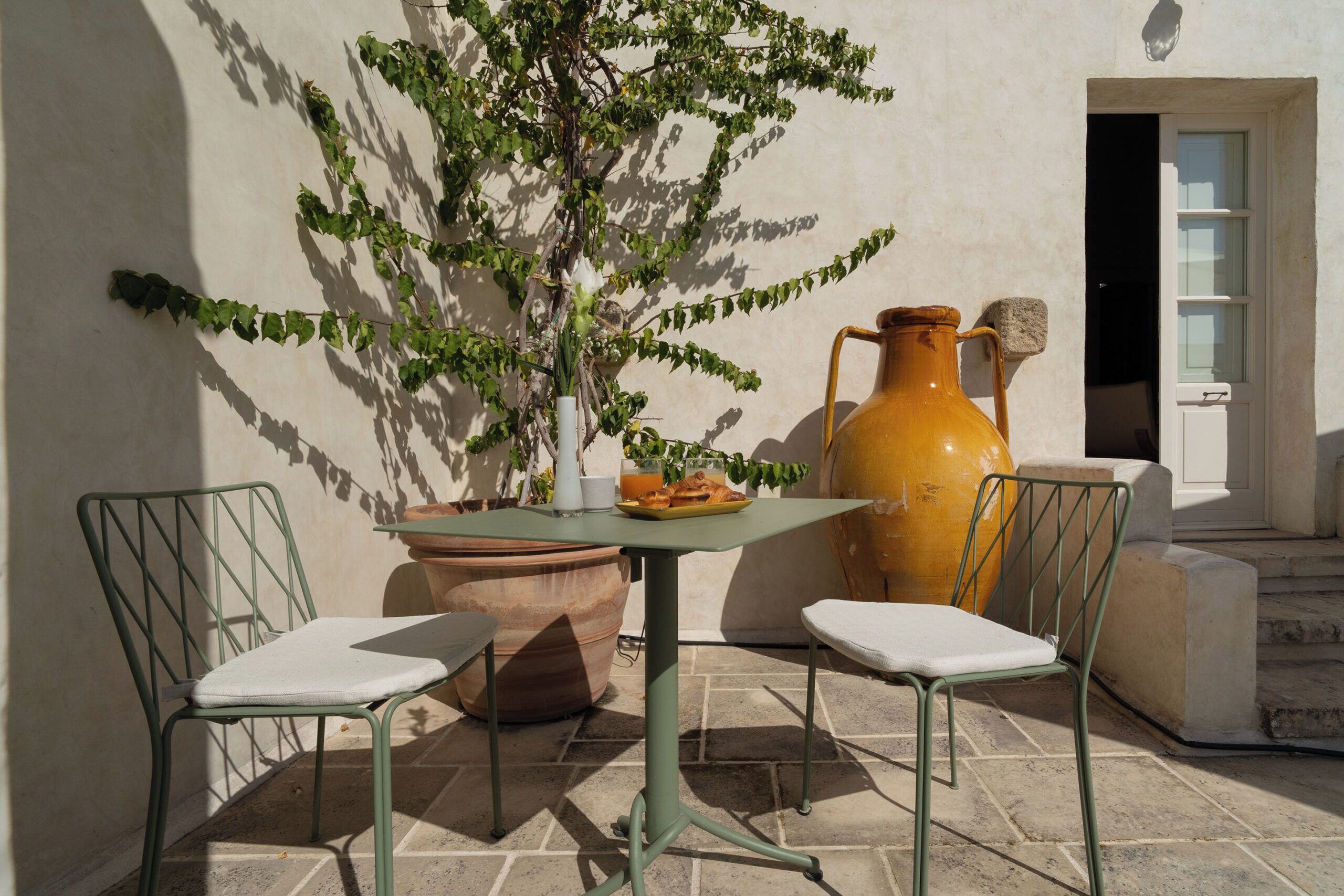 Eine Terrasse mit Tisch, zwei Stühlen, einer großen Vase und einem Blumentopf.
