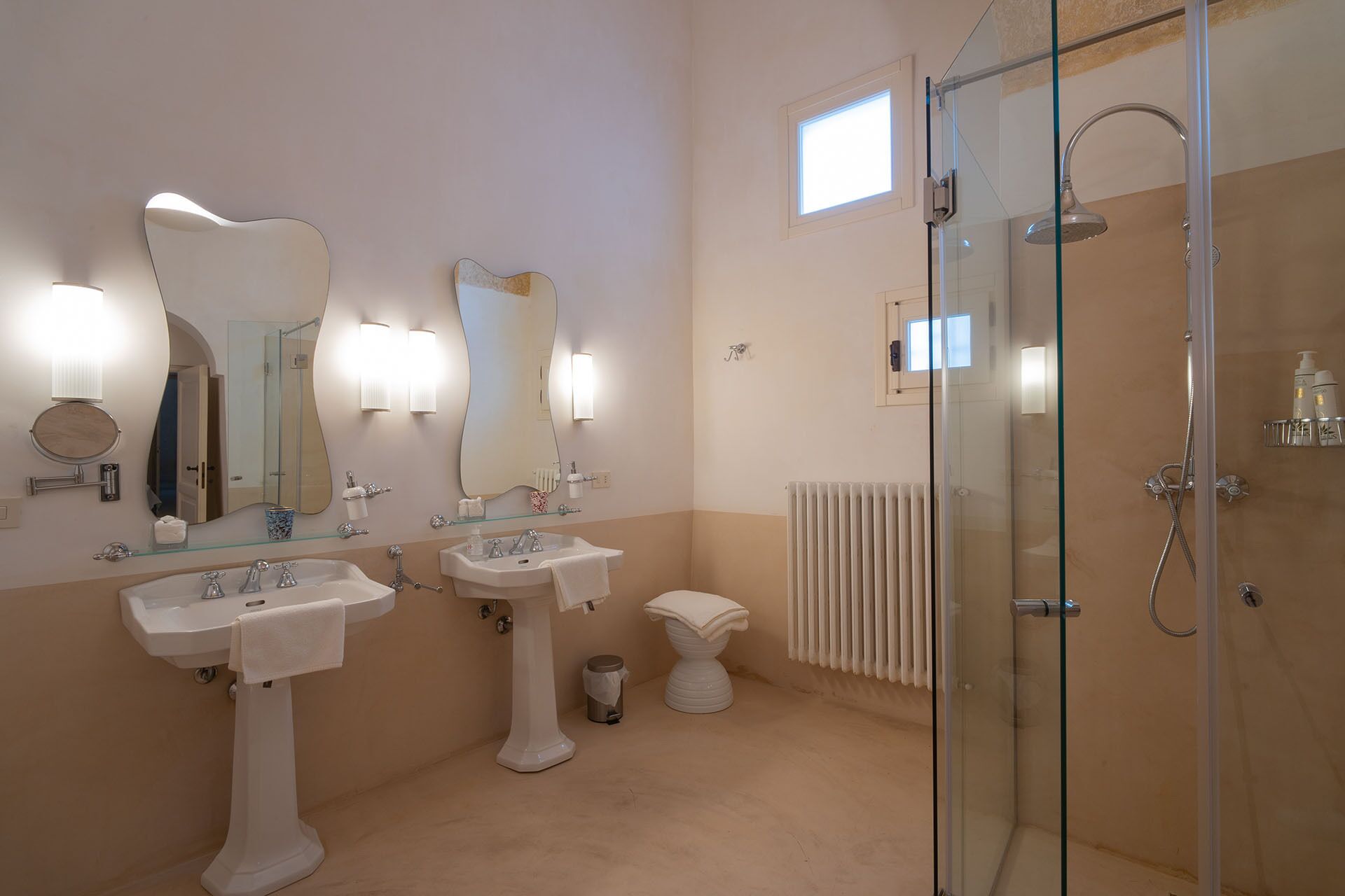 Een badkamer met twee wasbakken, toilet, douchecabine van glas en een radiator.