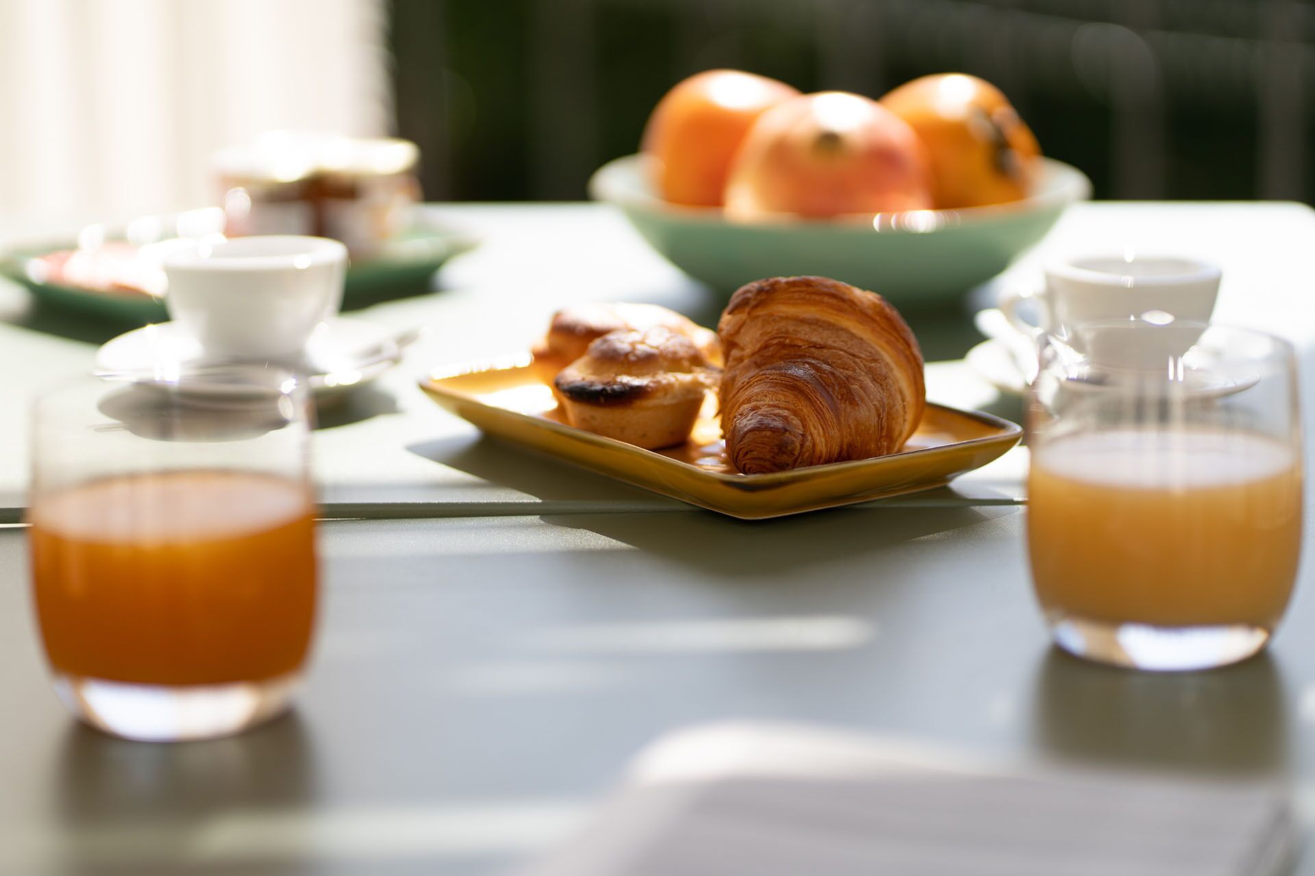 Una tavola per la colazione con croissant, una ciotola di arance e due bicchieri di succo d'arancia.
