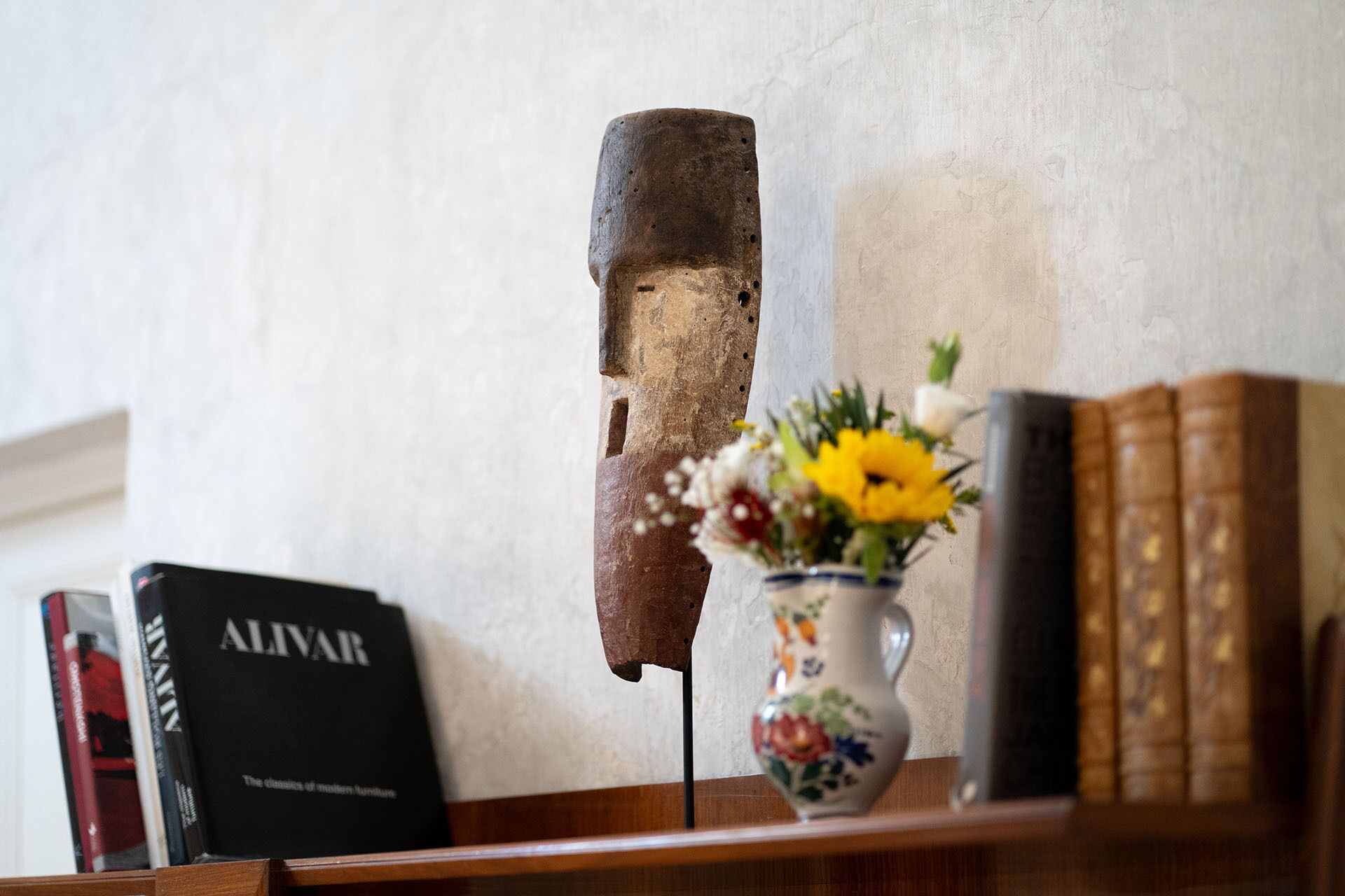 A bookshelf with books, a vase with flowers, and a rustic object.