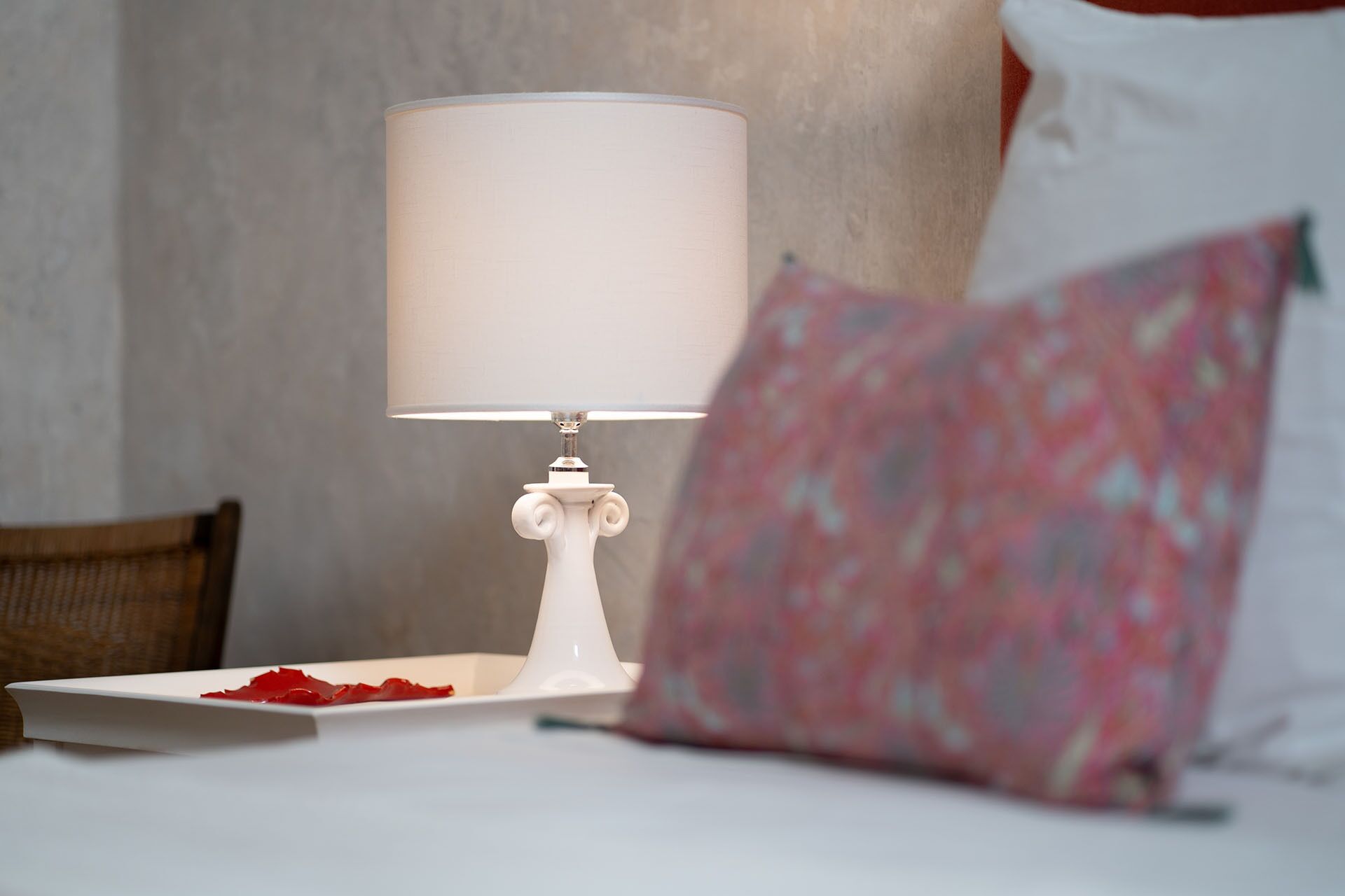 Een bed met een witte lamp en een sierkussen.