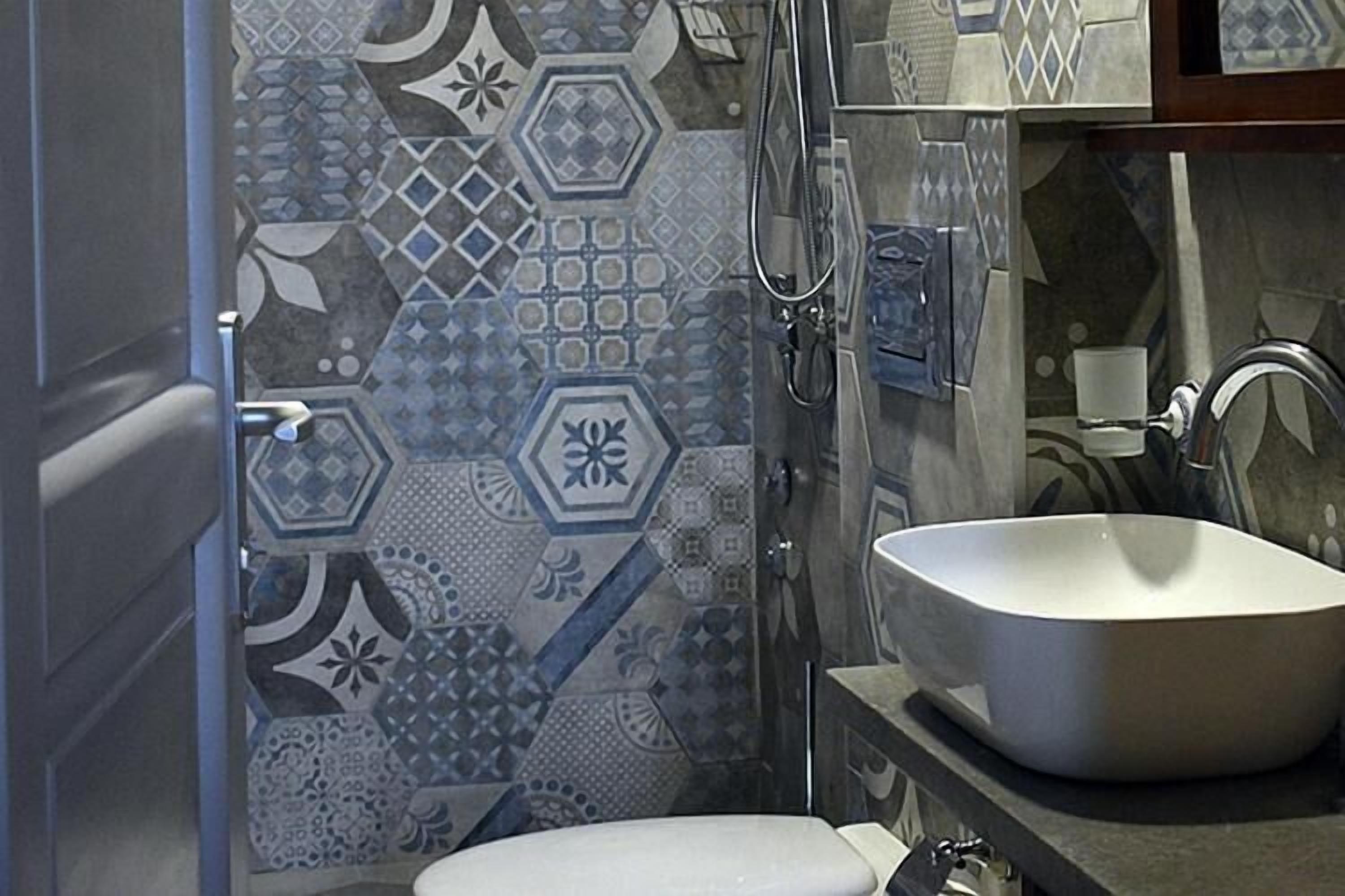 A bathroom with a white sink, a shower, and a toilet. The walls are tiled with a geometric pattern.