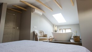 A bedroom with a skylight, a bathtub, a chair, and a bedside table with a lamp. - Villa Lav (Bale)