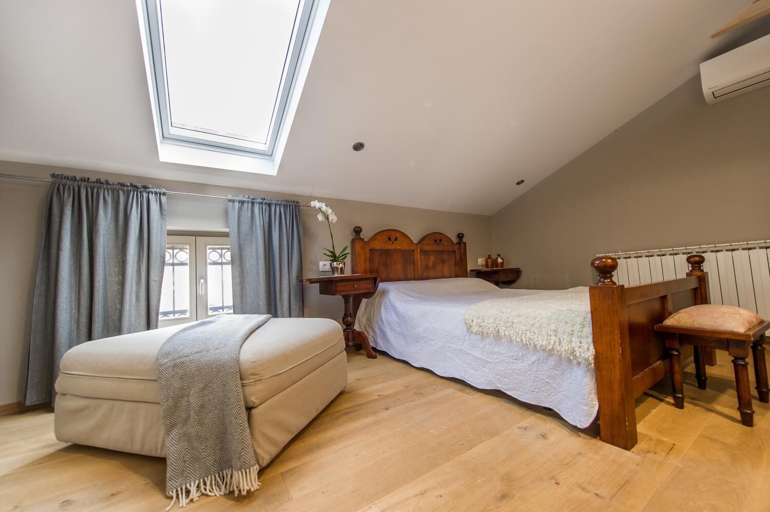 Une chambre avec un puits de lumière, un lit, un canapé et une tête de lit en bois.