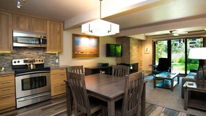A modern kitchen with a dining area, featuring a large wooden table, dark wooden chairs, a built-in oven, and a stone backsplash. - Lift One - Recently renovated one bedroom with patio (Aspen)