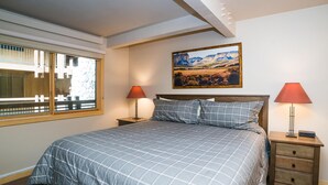 A bedroom with a large bed, two bedside tables, a window, and a painting on the wall. - Lift One - Recently renovated one bedroom with patio (Aspen)
