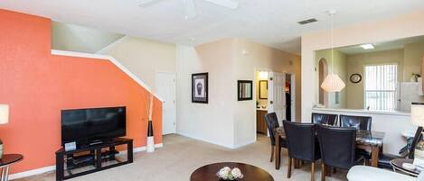 A living room with a TV, a dining area with chairs, a white sofa, and a ceiling fan.