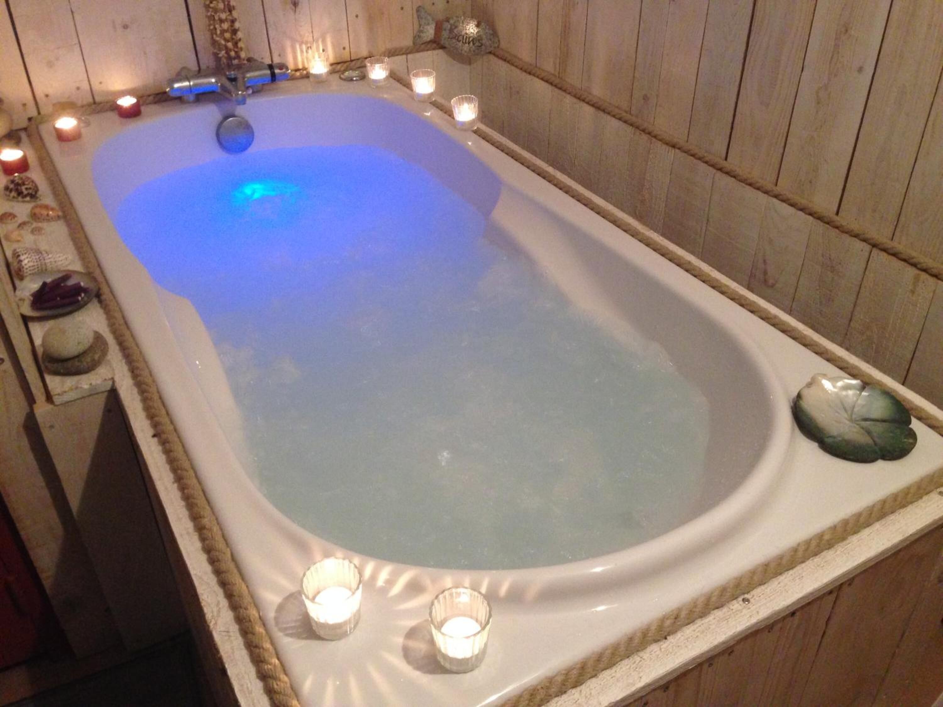 A large, rectangular hot tub with a wooden interior, surrounded by candles and decorative items.