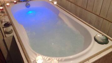 A large, rectangular hot tub with a wooden interior, surrounded by candles and decorative items.