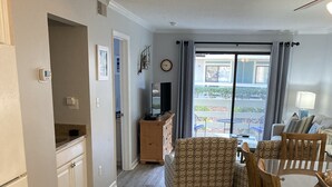 A spacious living area with a dining table and chairs, a built-in kitchen, and a large window with curtains. - Very Desirable 1st Floor Villa at Fiddler's Cove Beach & Racquet Club (Hilton Head Island)