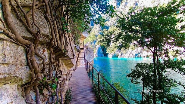 A wooden staircase leading down to a turquoise body of water, surrounded by rocky cliffs and greenery.