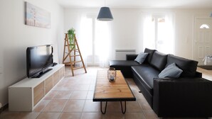 A living room with a TV, a wooden ladder with a plant, a black sofa, and a wooden coffee table.